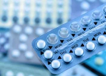 Oral contraceptive pill on pharmacy counter with colorful pills strips background.