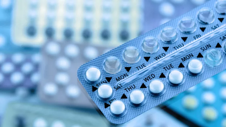 Oral contraceptive pill on pharmacy counter with colorful pills strips background.