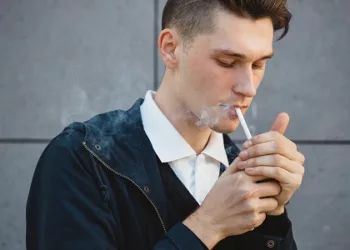 Fashion hipster male model smoking cigarette on the street