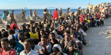Cientos de migrantes, procedentes de Marruecos, fueron fotografiados haciendo fila en una playa de Ceuta para recibir ayuda.